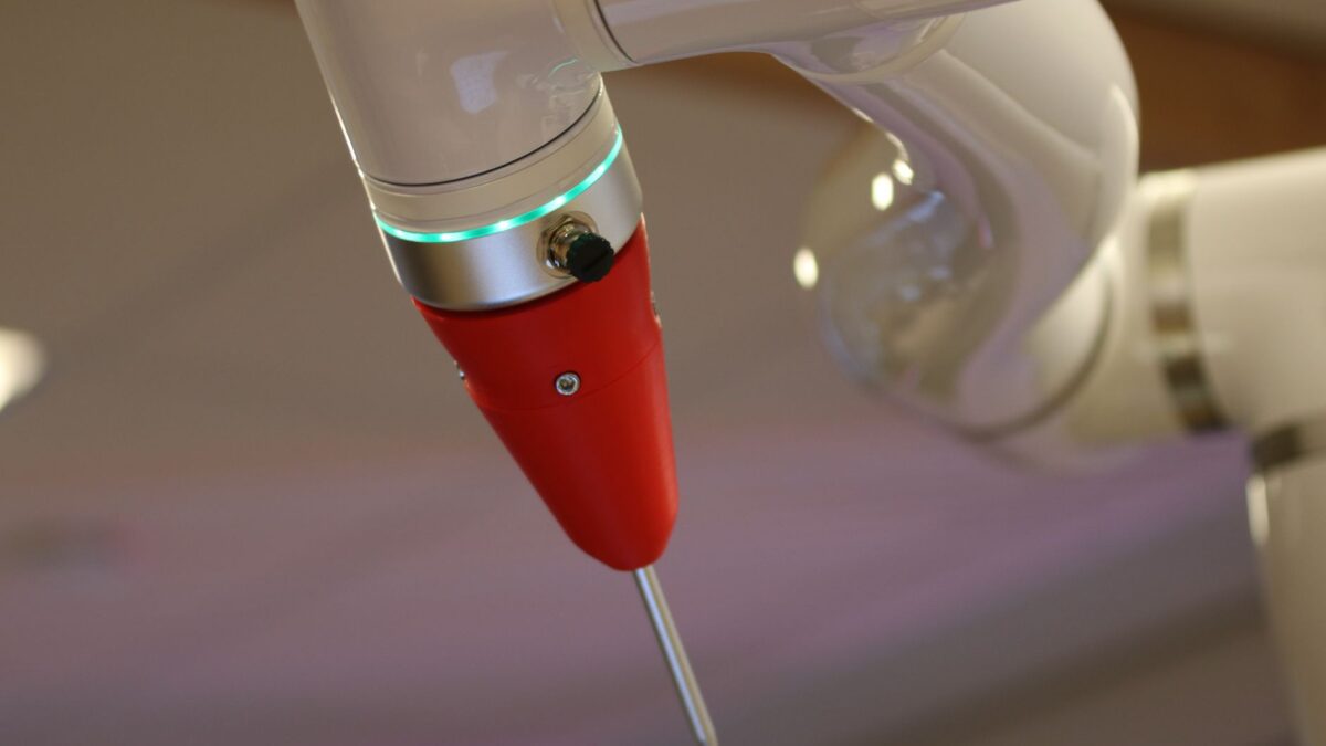 Bras robotique blanc avec pointe rouge et anneau lumineux vert effectuant une tâche précise.
