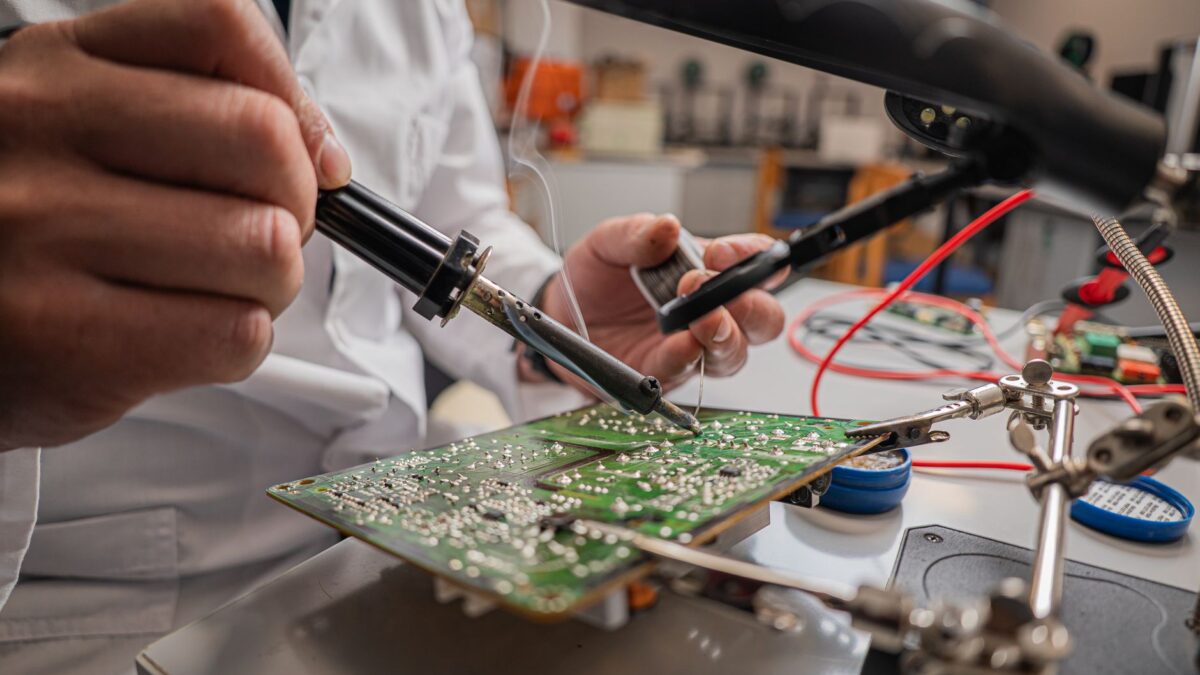 A skilled technician soldering electronic components on a green circuit board in a laboratory.