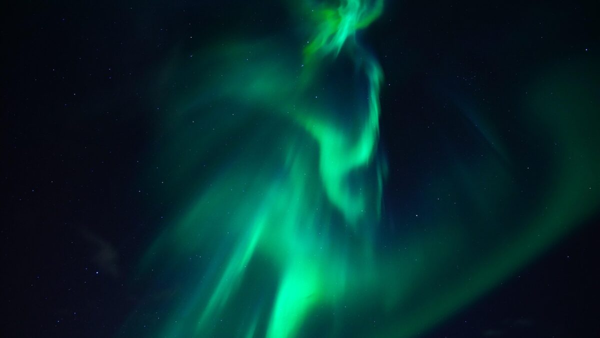 Aurore boréale verte ondulant dans un ciel nocturne étoilé, sans horizon ni présence humaine visible.