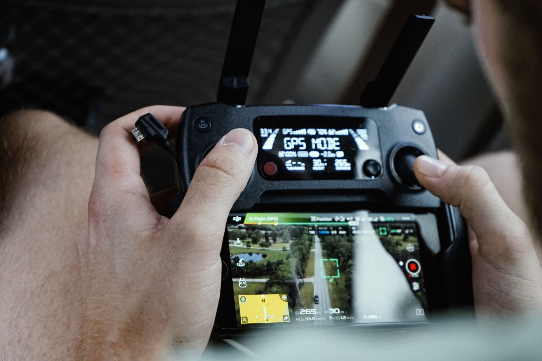 Close-up of hands operating a drone controller with a smartphone attached showing flight data.