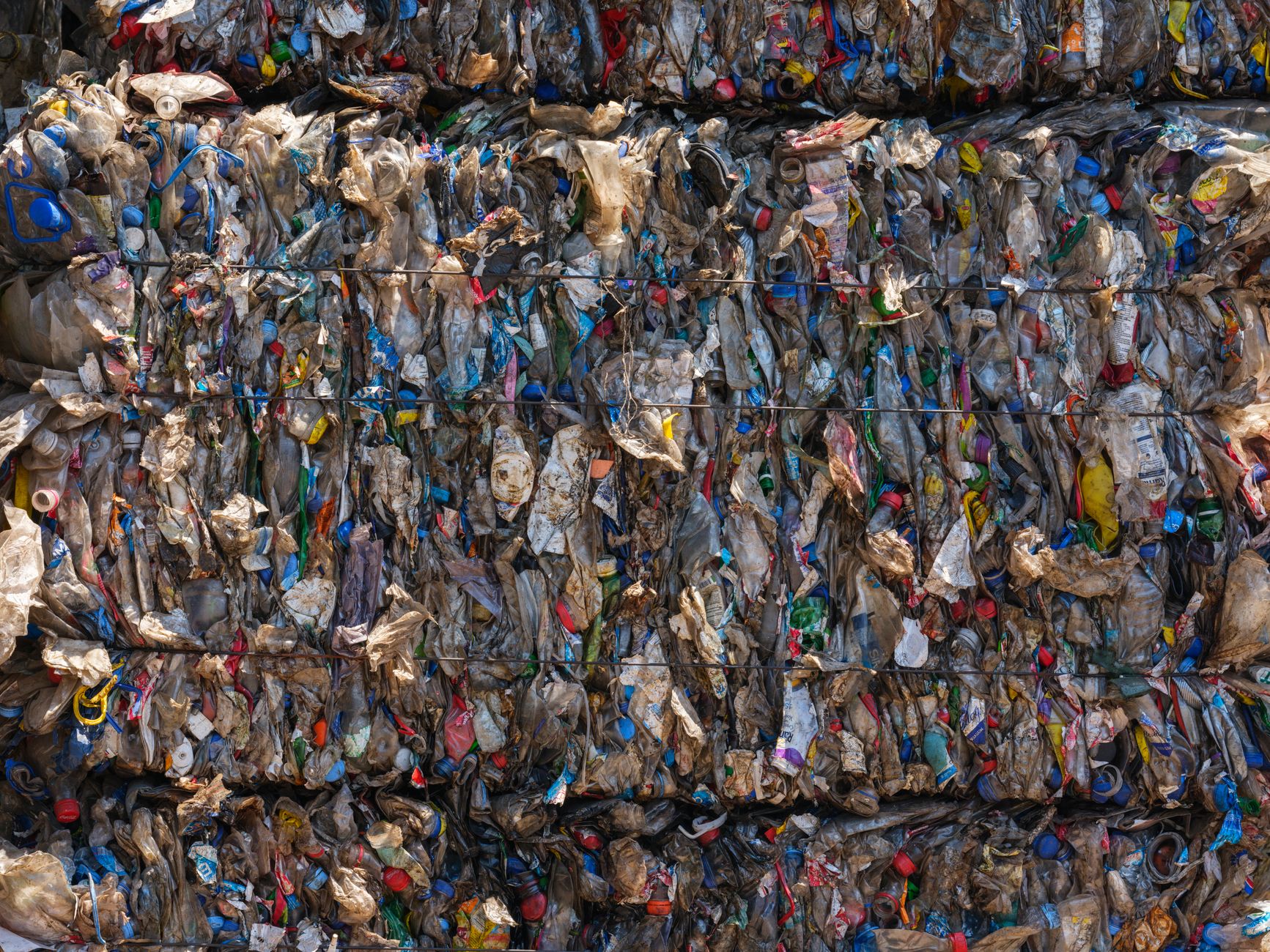 Stacked bales of crushed plastic bottles and packaging held together with metal wire, filling the frame.